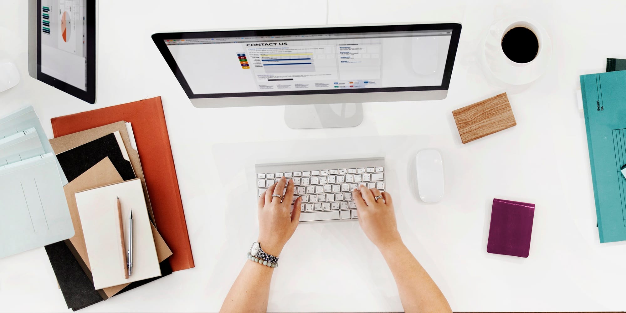 Mână pe tastatură în fața unui monitor cu o pagină web, pe un birou alb